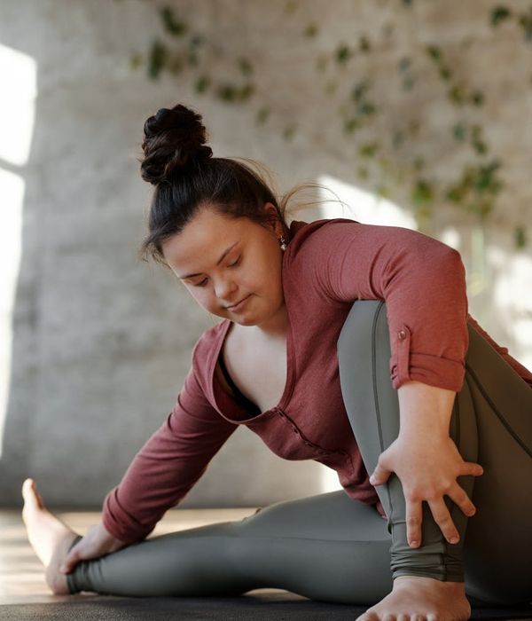 Woman in a calm, flowing yoga pose in a dark room with purple light.